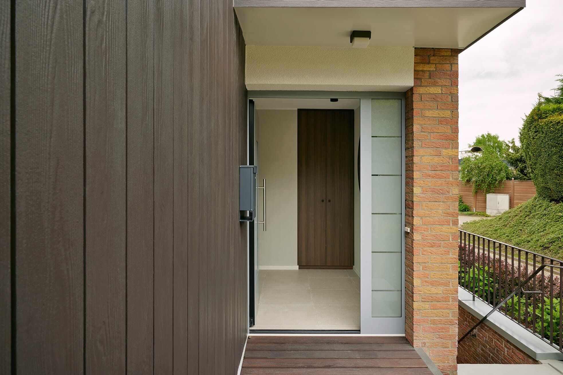 Nahaufnahme der Haustür mit Holz-Sidelight, dunkler Cladding-Wand und Klinkerpfeiler