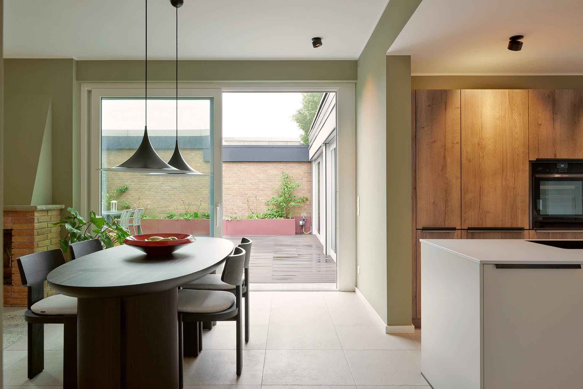 Esstisch mit Polsterstühlen und schwarzen Pendelleuchten, im Hintergrund die offene Küche